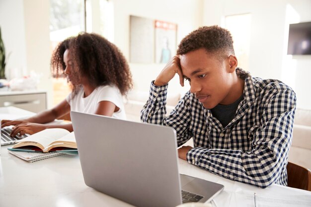 Irmão e irmã adolescentes negros trabalhando em laptops em casa