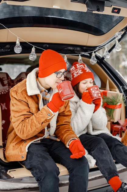 Foto irmão e irmã adolescentes sentados no porta-malas do carro aberto em winter park