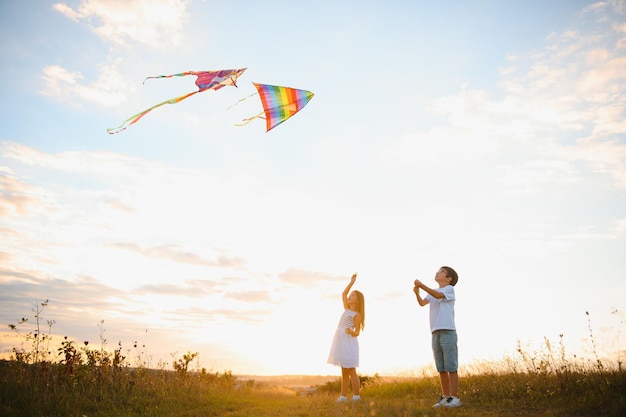 Irmão e irmã brincando com pipa e avião no campo ao pôr do sol