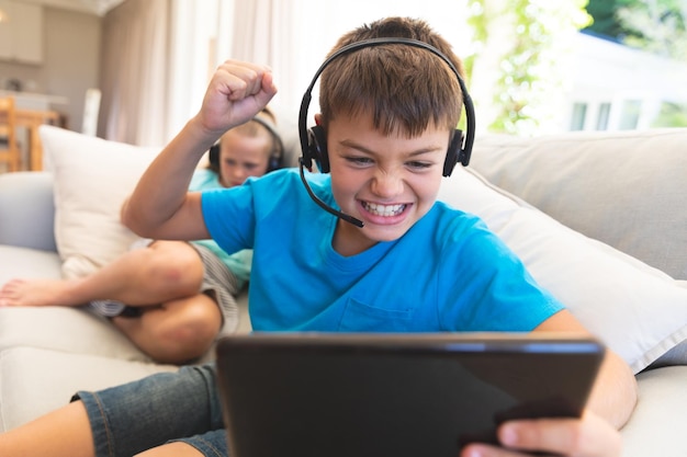 Foto irmão e irmã caucasianos usando fones de ouvido e tablets em casa. infância com tecnologia, passando o tempo livre em casa.