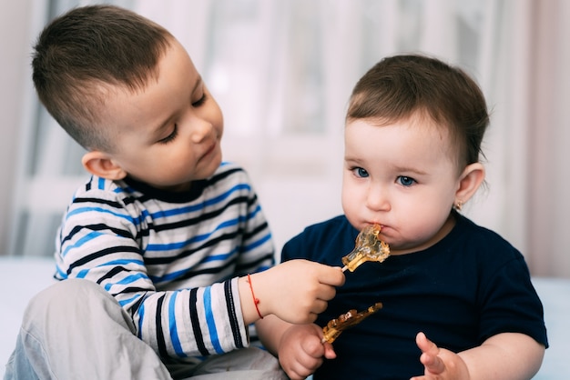 Irmão e irmã comem pirulitos em forma de galo, irmão dá para provar seu pirulito
