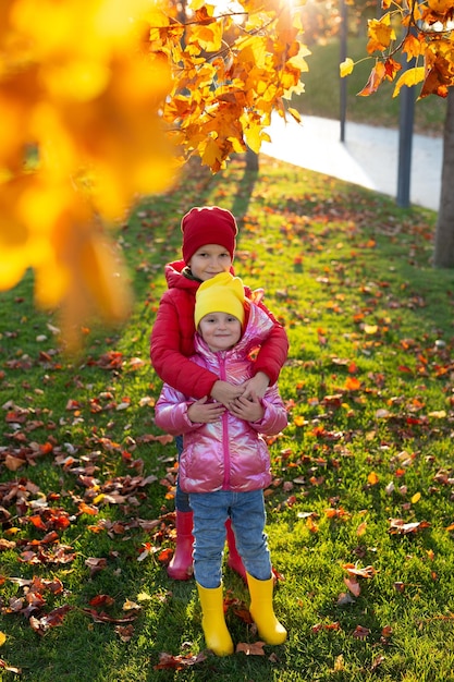 Irmão e irmã de crianças pequenas em botas de borracha e roupas brilhantes no parque de outono