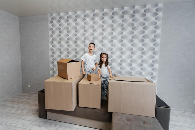 Irmão e irmã estão brincando e gostando de se mudar para um novo apartamento no contexto de caixas de papelão no sofá Compra de imóveis Entrega de inauguração de casa