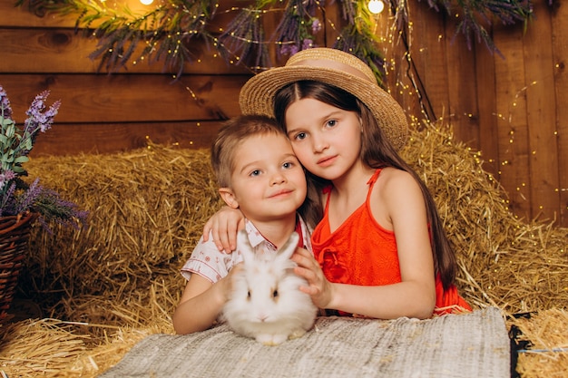 Irmão e irmã felizes abraçam um coelho na aldeia no feno