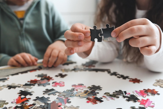 Irmão e irmã jogando quebra-cabeças em casa crianças conectando peças de quebra-cabeça em uma mesa da sala crianças montando um quebra-cabeça lazer divertido em família