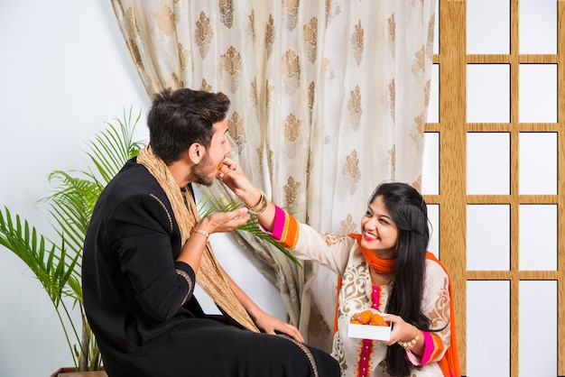 Irmão e irmã mais novos indianos celebrando o festival Raksha Bandhan ou Rakhi ou no Bhai dooj ou Bhau-Beej com Poja Thali, doces, presentes ou tirando fotos de selfies