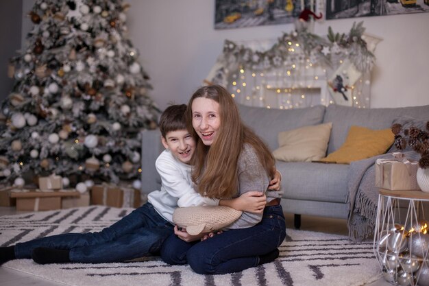 Irmão e irmã sentados no chão perto da árvore de natal