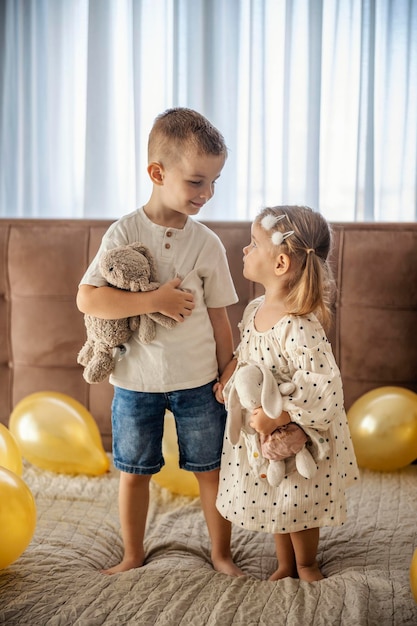 Irmão feliz e sua irmãzinha de pé cercados por balões e olhando um para o outro