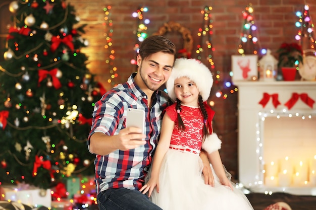 Irmão mais velho e irmã mais nova tirando fotos com o smartphone na sala de estar de natal