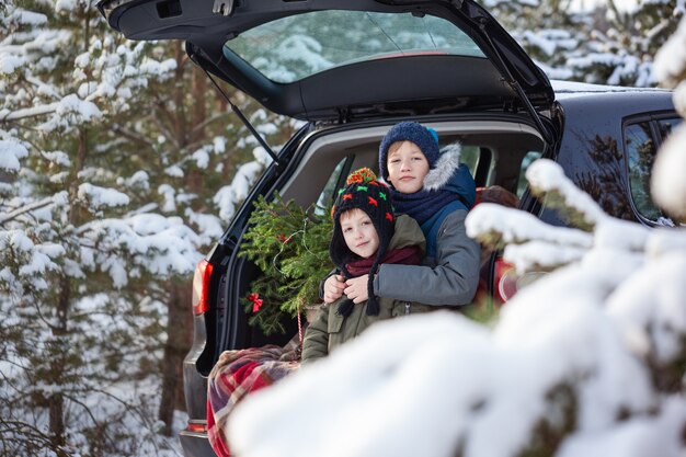 Irmãos adoráveis sentados no carro na floresta de neve de inverno