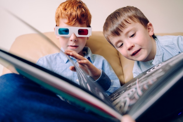 Irmãos alegres que leem um livro junto com os vidros 3d. Livros educacionais e atividades de aprendizagem para crianças intelectualmente ativas que compartilham atividades de lazer em casa.