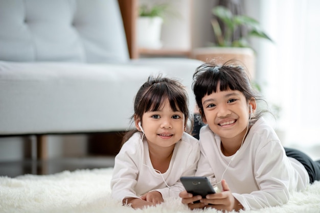 Irmãos asiáticos juntos no chão usando smartphone