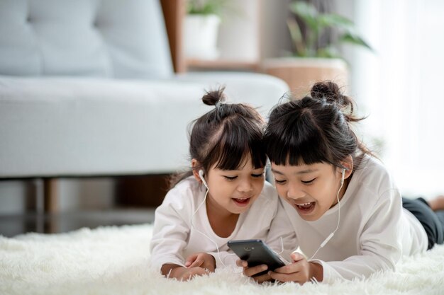 Irmãos asiáticos juntos no chão usando smartphone