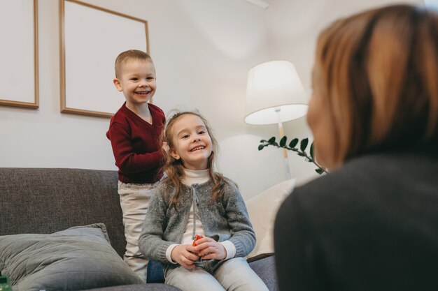 Irmãos caucasianos se divertindo com a mãe, sentados no sofá e sorrindo