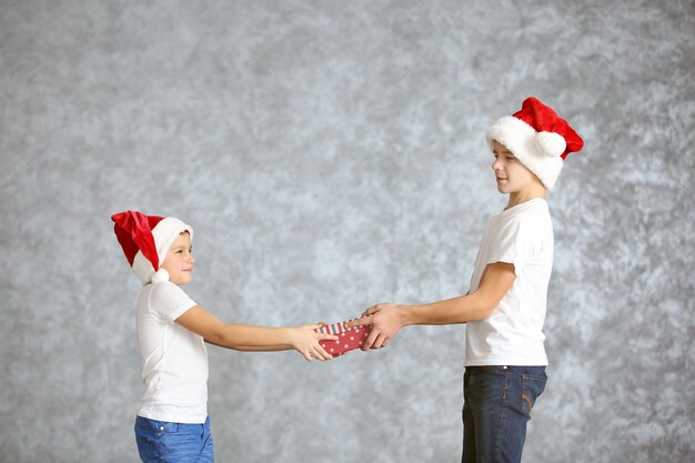 Irmãos com gorros de Papai Noel com caixa de presente na superfície cinza