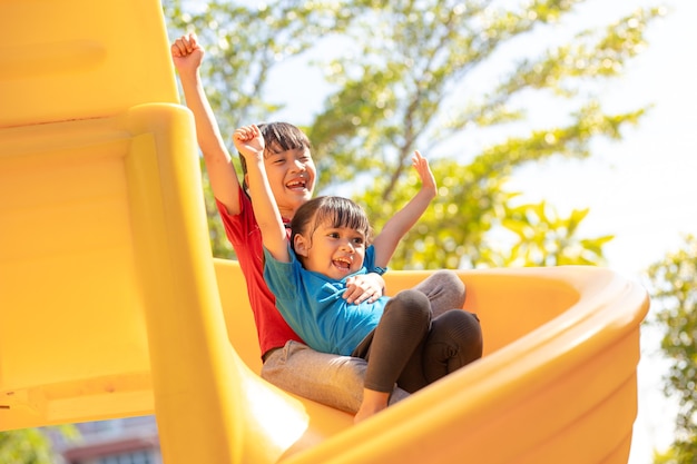 Foto irmãos de meninas bonitos se divertindo no playground ao ar livre em um dia ensolarado de verão. crianças em slides de plástico. atividade divertida para criança. lazer esporte ativo para crianças