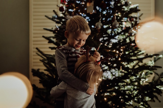 Irmãos de pé contra a árvore de Natal em casa