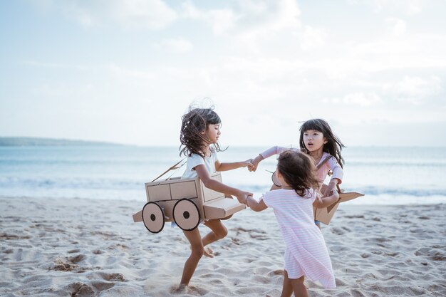 Irmãos e amigas brincando com um avião de papelão e um carro na praia