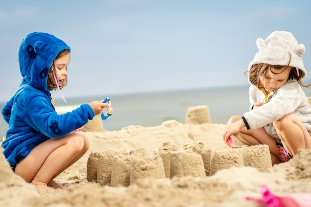 Irmãos fazendo castelos de areia enquanto se agacham na praia