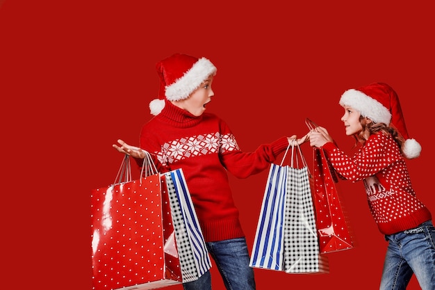 Irmãos fofos com suéter vermelho segurando sacolas de compras