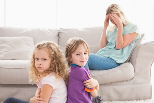 Irmãos irritados sentados braços cruzados com mãe triste no sofá