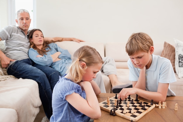 Irmãos jogando xadrez na frente de seus pais