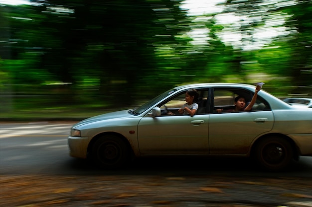 Irmãos se divertindo em um carro em movimento na estrada contra árvores