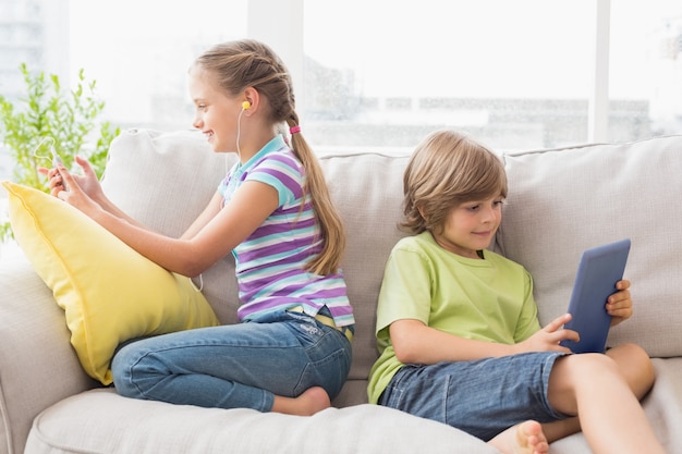 Irmãos usando tecnologias no sofá