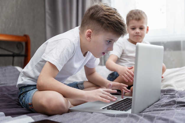 Irmãozinhos estão sentados em casa na frente de um laptop. Ensino à distância.