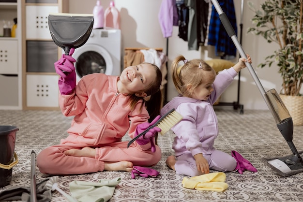 Foto irmãs ajudam seus pais a limpar sua nova casa duas meninas adoráveis com um balde de esfregão e material de limpeza se preparam para limpar o banheiro e brincar conceito de mudança e limpeza de residência