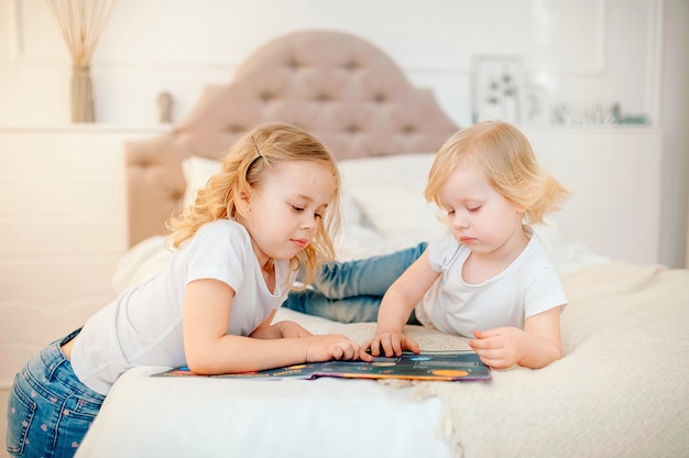 Irmãs de menina bebê loiro europeu ler um livro na cama