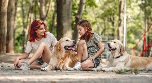Irmãs de meninas com cães golden retriever sentados no parque. Família com cachorrinhos ao ar livre