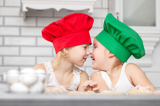 Irmãs em chapéus de cozinheiro brilhante assando juntos em uma cozinha
