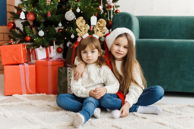 Foto irmãs fofas estão sentadas no interior do natal e comemorando o natal e o ano novo
