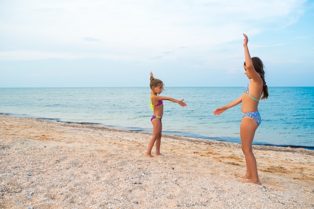 Irmãs garotinhas positivas jogam jogos ativos na praia durante as férias de verão em um dia ensolarado de verão quente. O conceito de descanso do inverno e da cidade