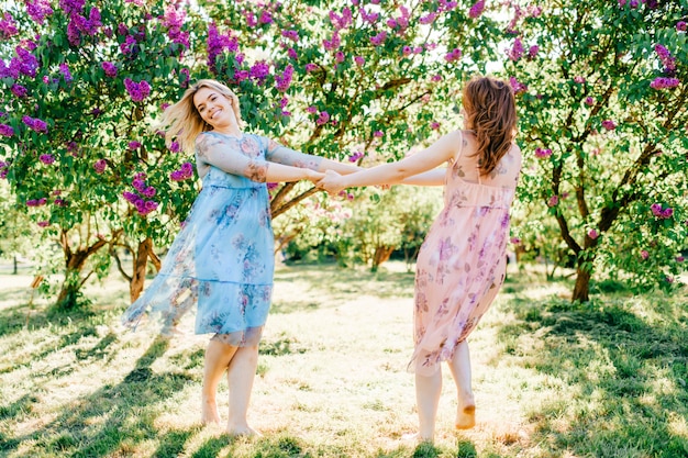 Irmãs gêmeas felizes fofos em vestidos bonitos, girando no parque de verão florescendo.