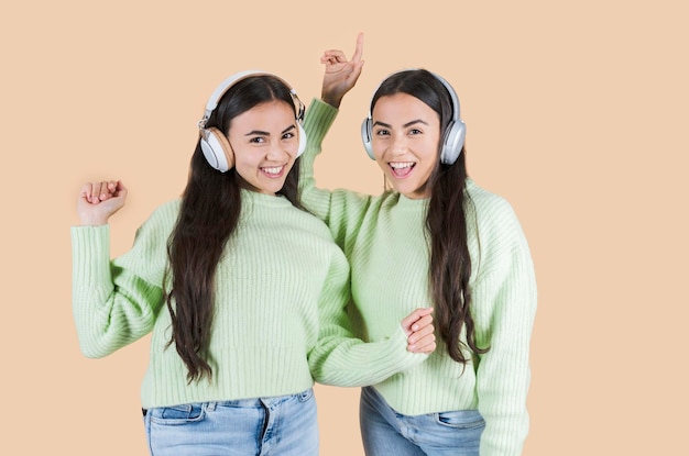 irmãs gêmeas ouvem música fones de ouvido estúdio fundo bege
