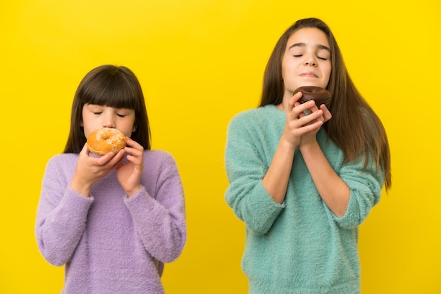 Irmãs mais novas isoladas em um fundo amarelo segurando uma rosquinha