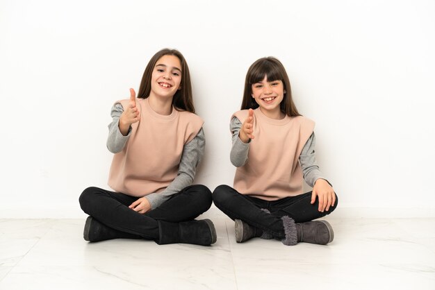 Irmãs mais novas sentadas no chão isoladas apertando as mãos para fechar um bom negócio