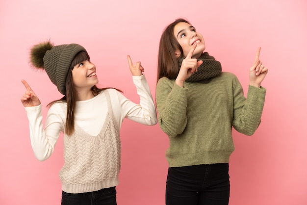 Irmãs mais novas vestindo roupas de inverno isoladas em um fundo rosa apontando com o dedo indicador uma ótima ideia