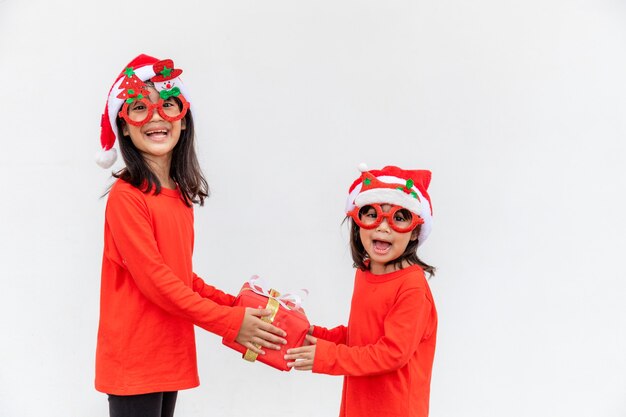 Irmãs meninas asiáticas com chapéu de Papai Noel vermelho com caixas de presente em fundo branco.