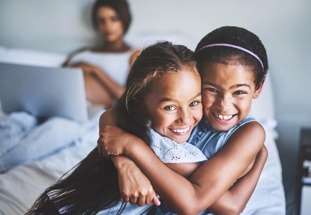 Irmãs para a vida Retrato de duas meninas alegres com os braços em volta enquanto sua mãe grávida relaxa em segundo plano com um laptop