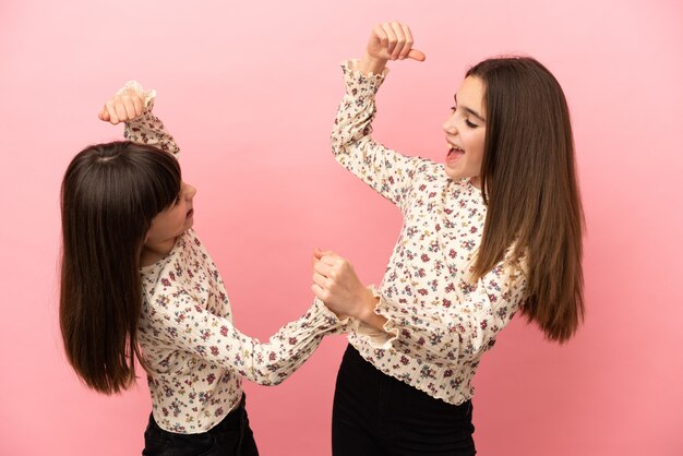 Irmãs pequenas isoladas em um fundo rosa comemorando a vitória na posição vencedora