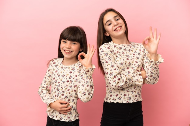 Irmãs pequenas isoladas em um fundo rosa mostrando um sinal de ok com os dedos