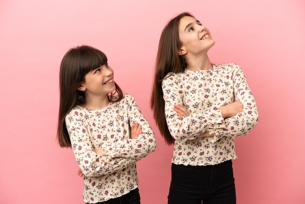 Irmãs pequenas isoladas em um fundo rosa olhando para cima enquanto sorriem