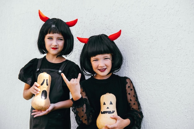 Irmãs usando peruca com chifres vermelhos e vestidos pretos no retrato da festa de comemoração do dia das bruxas parede branca para um fundo