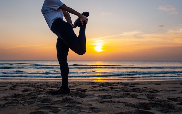 Irreconhecível jovem alongamento antes do treino na praia ao pôr do sol