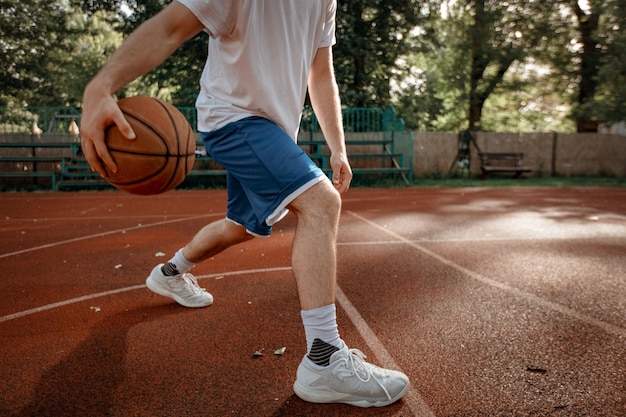 Irreconhecível jovem jogador de basquete de rua mostrando suas habilidades na quadra.