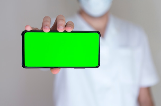 Irreconhecível médico segurando um smartphone com tela verde no hospital.