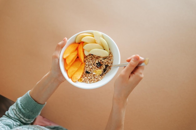 Irreconocible en las manos hermoso plato de desayuno jugosas rebanadas de fruta apetitosamente se encuentran en granola